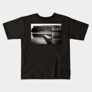 Black and white photograph of a wooden pier on a lake surrounded by a forest Kids T-Shirt